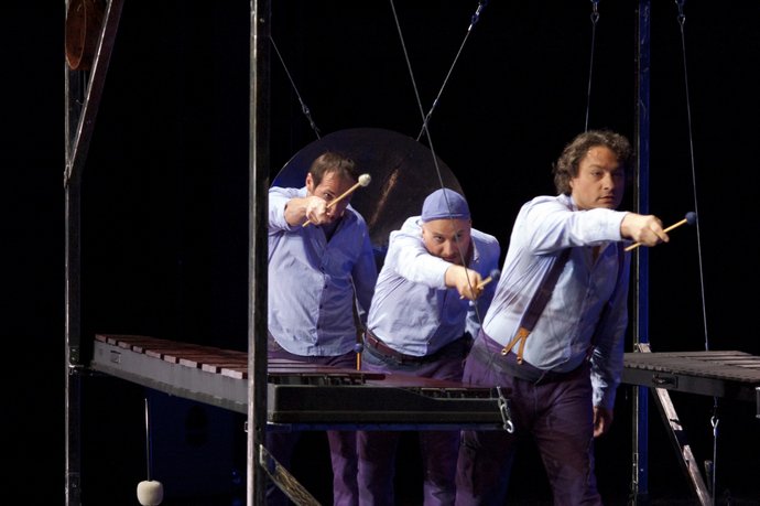 Das Kind der Seehundfrau. Foto aus dem Theaterstück, Fisch werfen: 3 Männer zeigen dynamisch mit ihren Xylophon-Sticks in Richtung des Fotografen