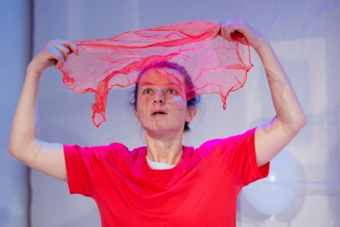 Frau in rotem T-Shirt hält erstaunt ein transparentes, rotes Tuch über dem Kopf, das zu schweben scheint.