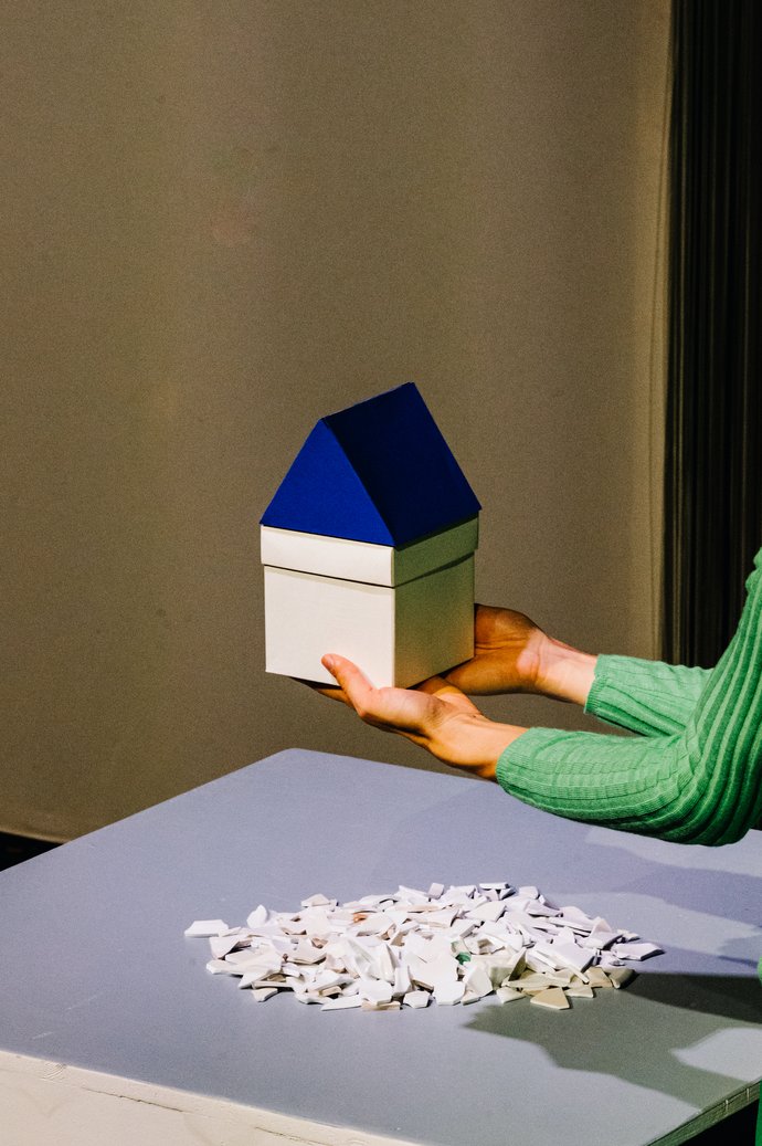 Eva hält ein kleines weißes Papp-Haus in den Händen mit blauem Dacht.