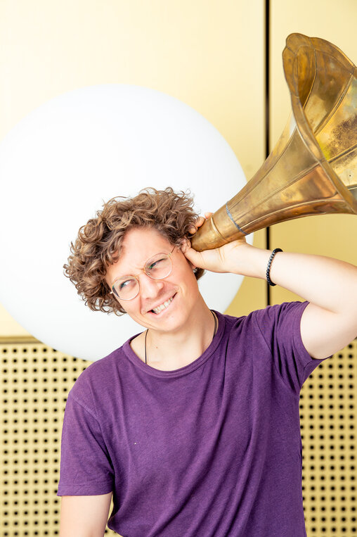 Dominik Vogl, musikalischer Leiter des Theater Pfütze vor der goldenen Theaterfassade hält sich goldenes Grammophon an Ohr