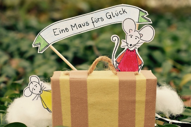 Eine Maus fürs Glück, eine kleine Papiermaus sitzt auf einem gebastelten Koffer aus Pappe